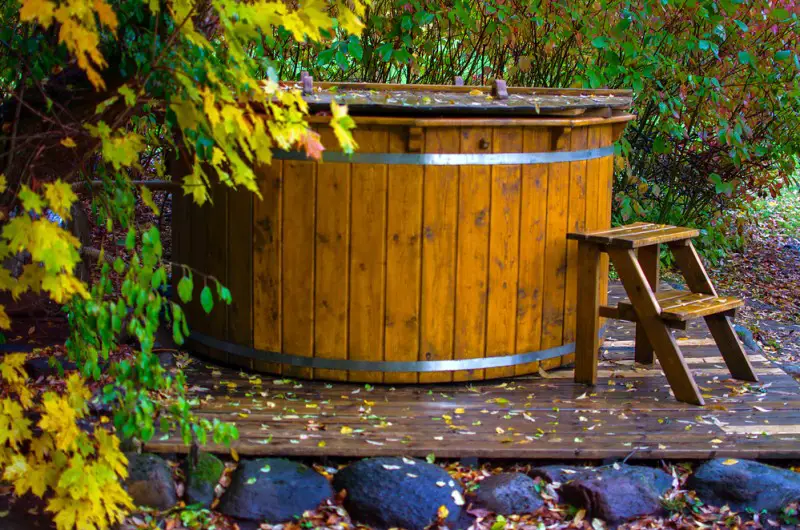 covered wooden hot tub with a ladder